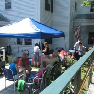 From left, volunteers Anna and Marie sit in the shade with residents, Ruth, Jeanne and Richard. Carl Overlock mans the grill and staff member Krista George looks on holding her son, Dominick, on the ramp. Courtesy photo